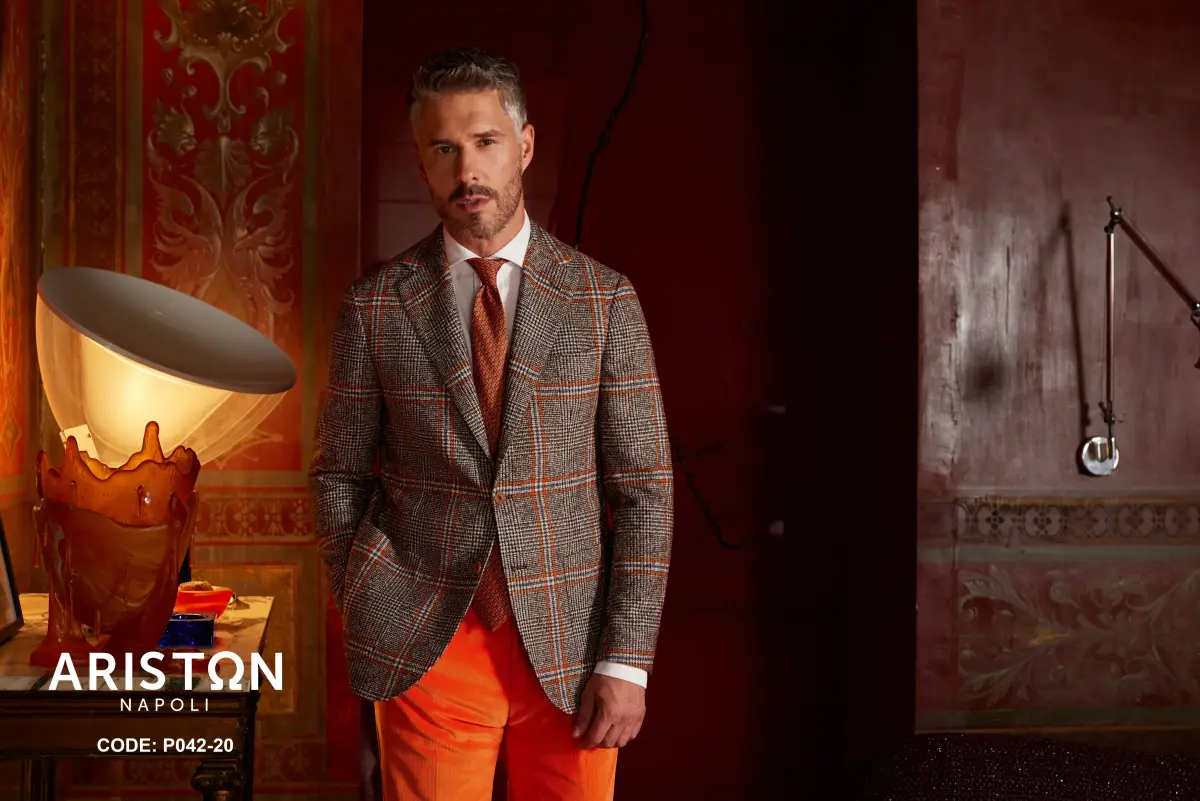 Brown tweed jacket with orange windowpane over a white shirt and textured orange tie, paired with vivid orange trousers—confident autumn tones
